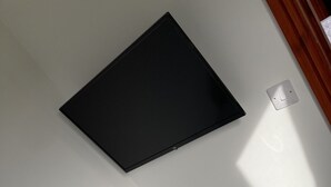 Une chambre avec un lit blanc, un téléviseur noir fixé au mur et un interrupteur.