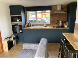 A compact kitchen with a built-in oven, a coffee machine, and a window with a view of parked cars.