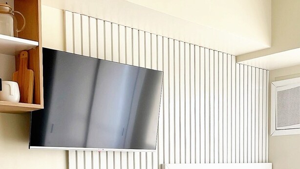 Une chambre d’hôtel moderne dotée d’un téléviseur à écran plat fixé au mur, d’un lit avec une tête de lit capitonnée et d’un coin repas avec un buffet.