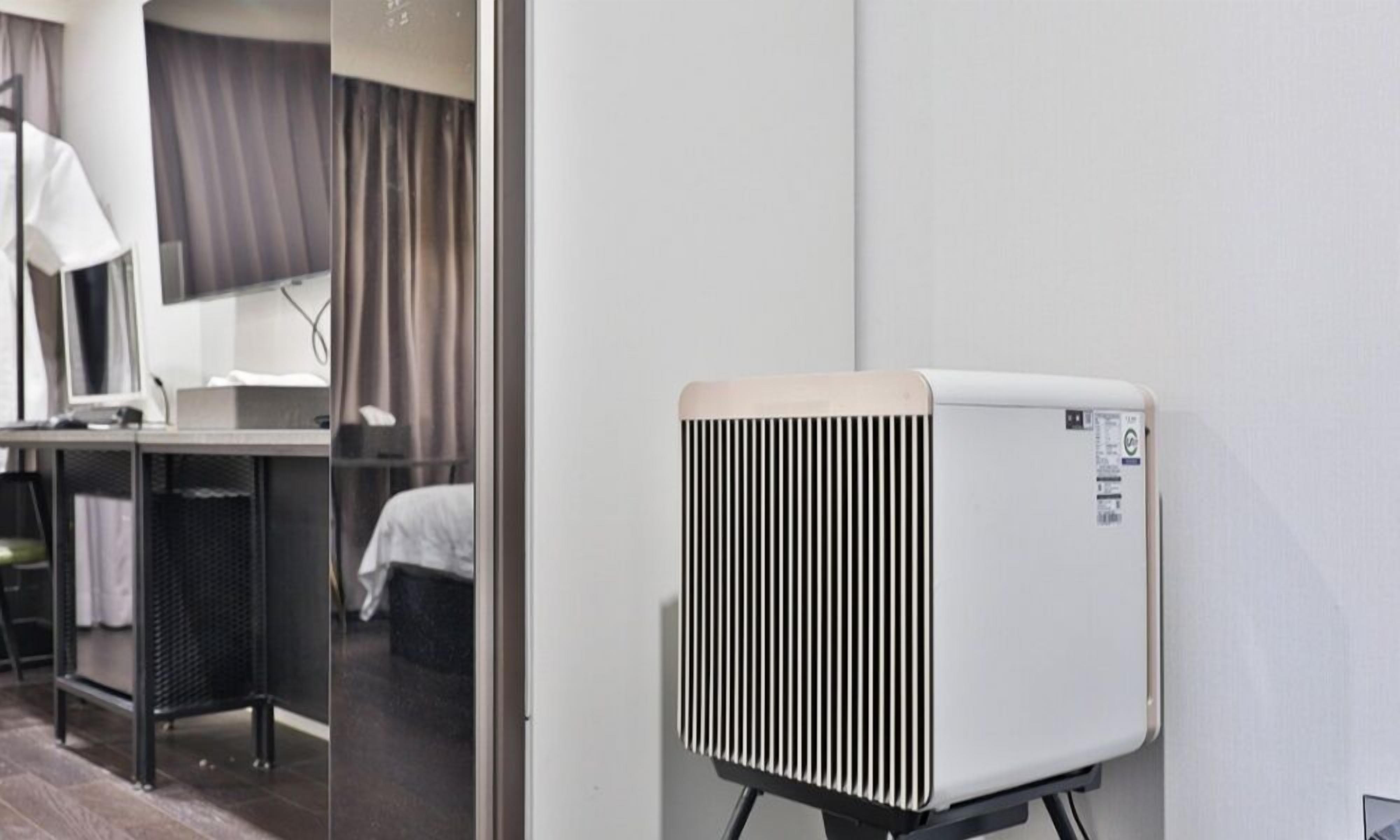 Een moderne hotelkamer met een elektrische kachel, een bureau met een lamp en een bed met een donker hoofdeinde.