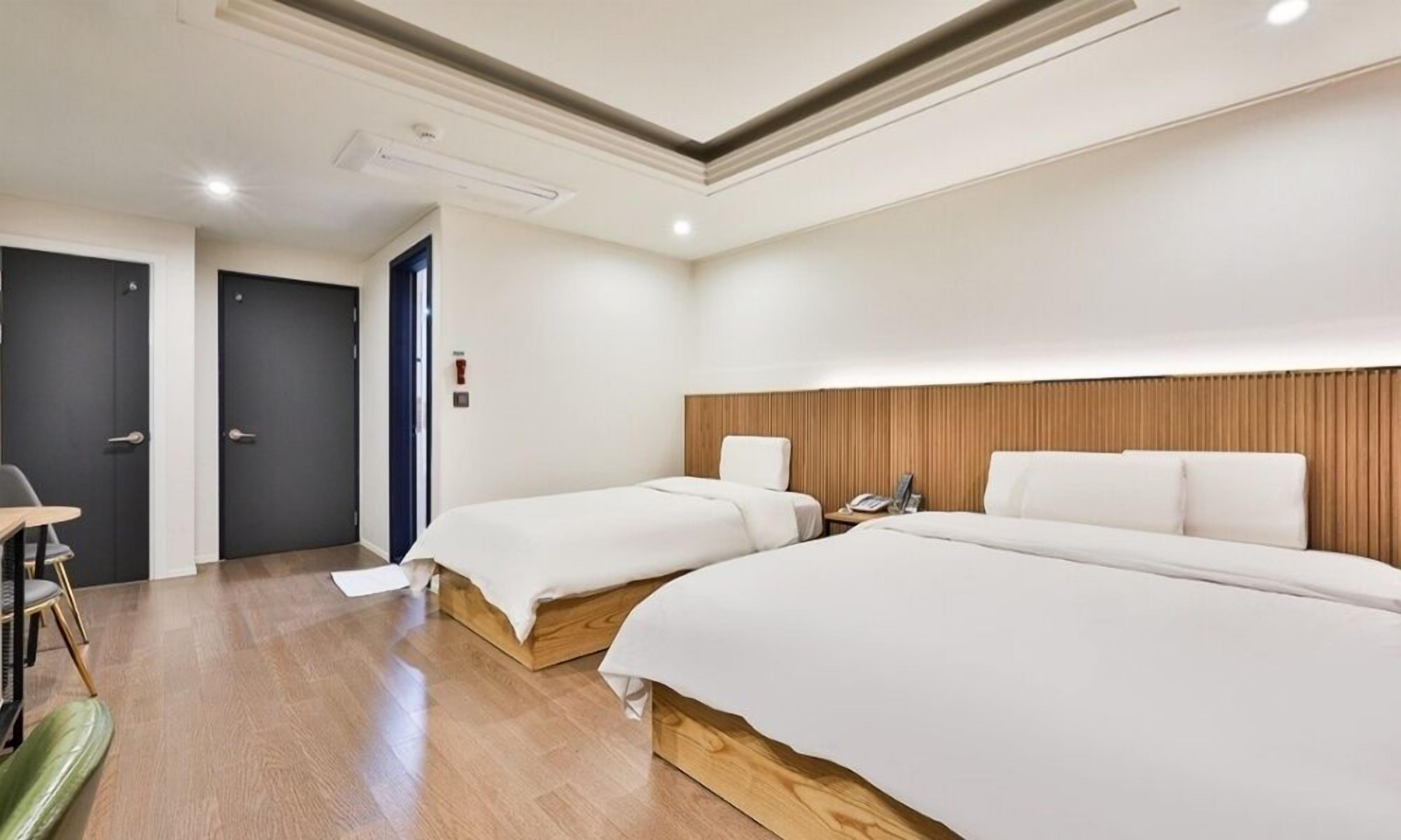 Una habitación de hotel con dos camas individuales, cabecera de madera, un escritorio y una silla.