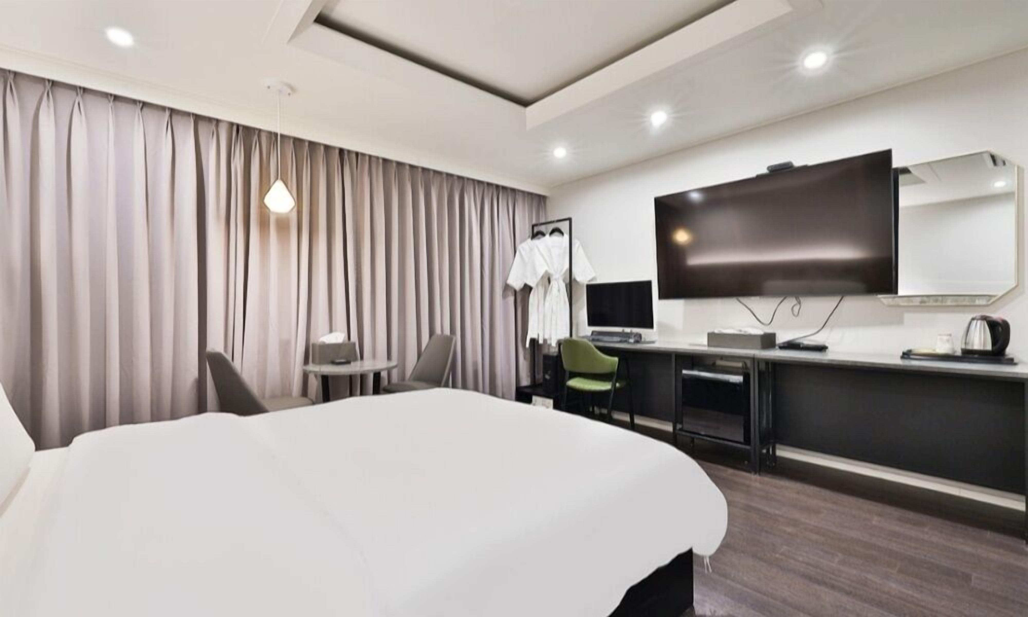 Et moderne hotelværelse med en stor seng, et skrivebord med et fladskærms-tv, en stol og et lille bord.