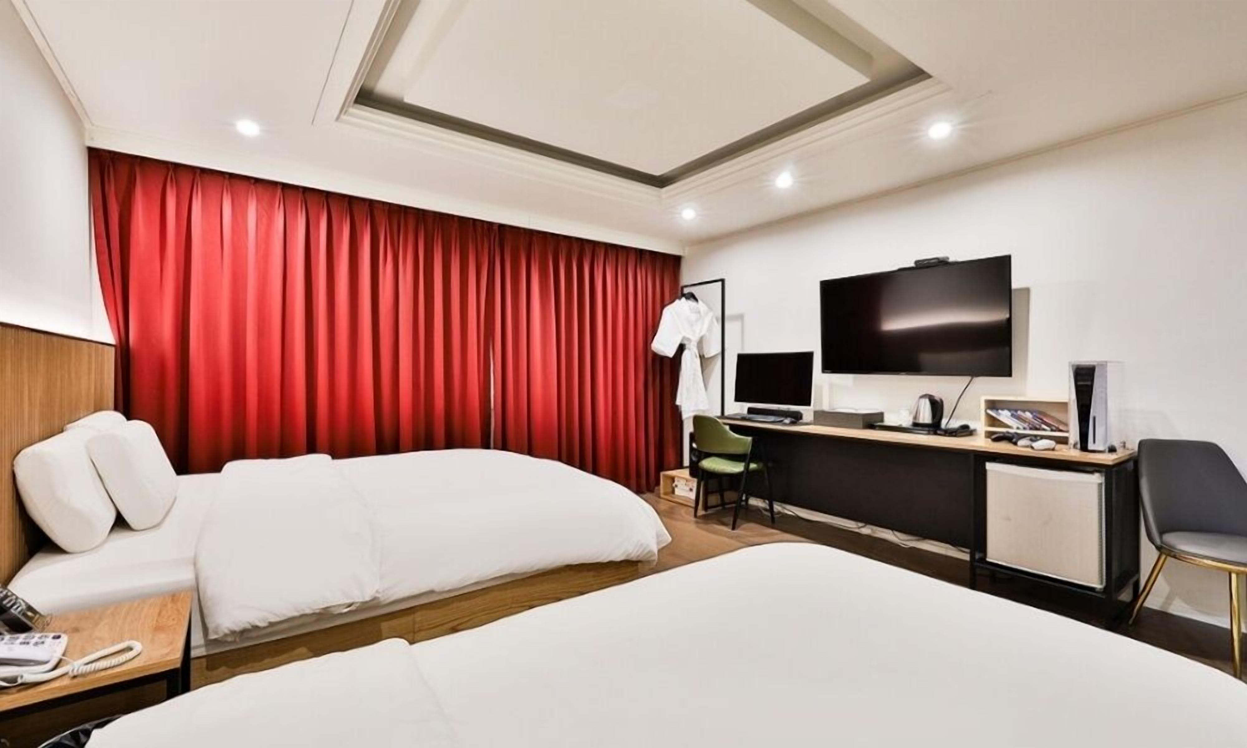 A hotel room with a large bed, a desk with a computer, a TV, and a red curtain.