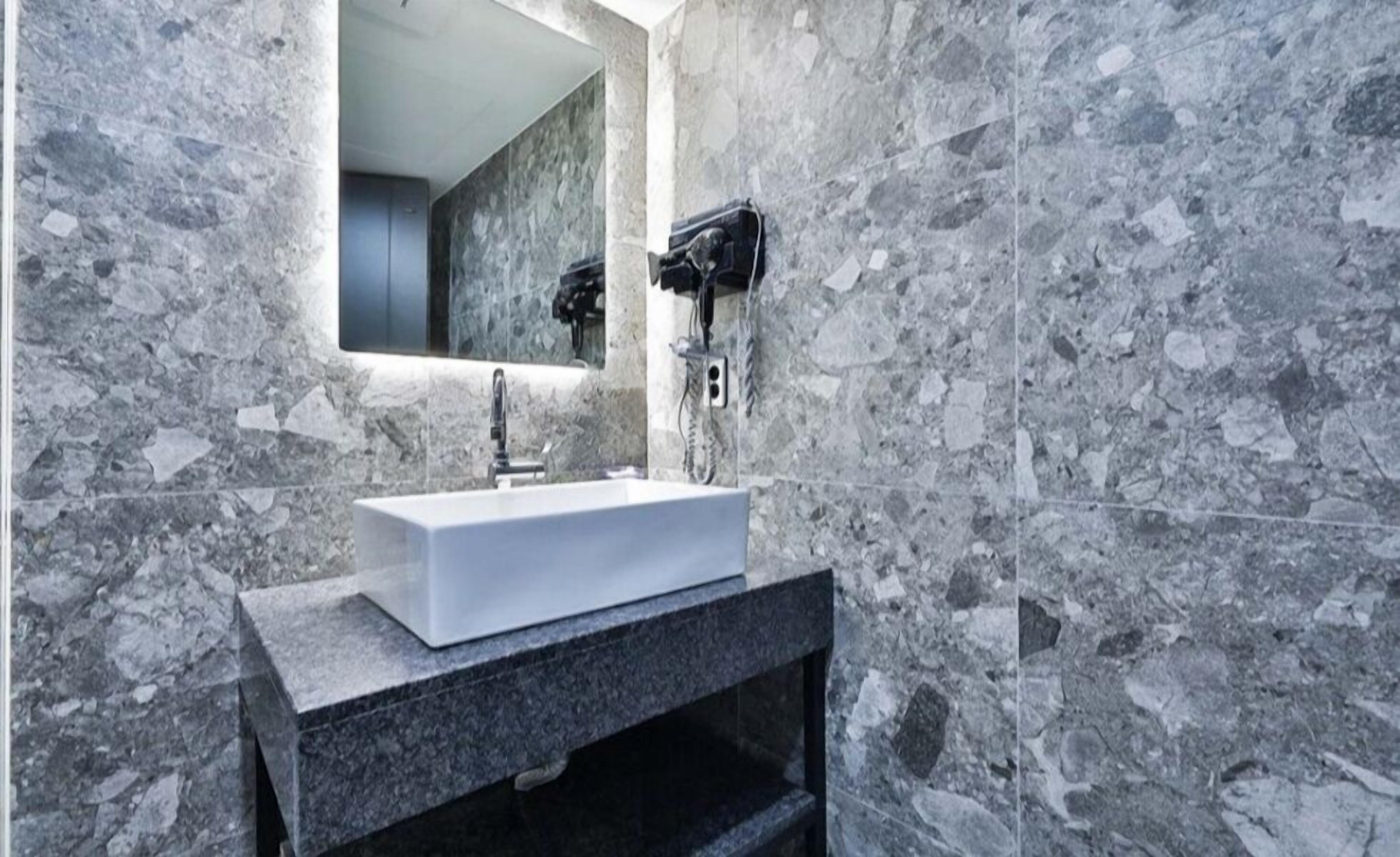 A bathroom with a white sink, a mirror, and a hairdryer mounted on the wall.