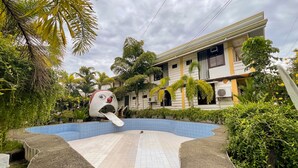 Una piscina de diseño único, rodeada de exuberante vegetación y un edificio con múltiples ventanas y balcones.