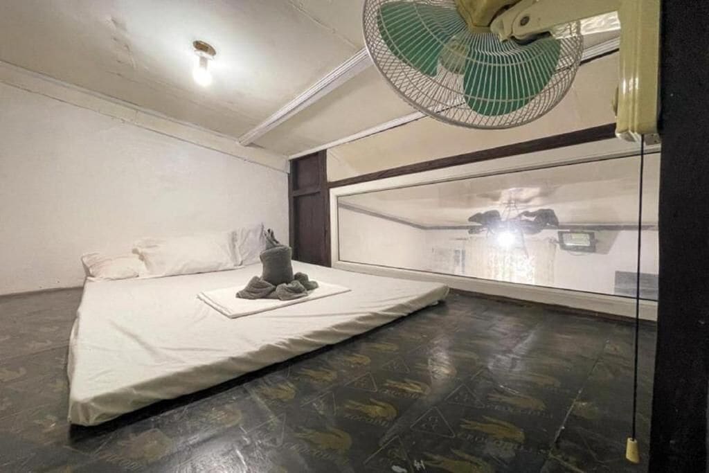A room with a bed, a fan, and a large window.