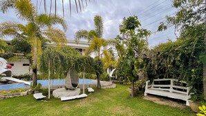Un jardín bien cuidado con una hamaca, un banco blanco y una pequeña piscina.