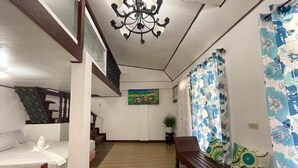 Una habitación de hotel con una cama de madera, un banco con cojines estampados, una araña y un cuadro en la pared.