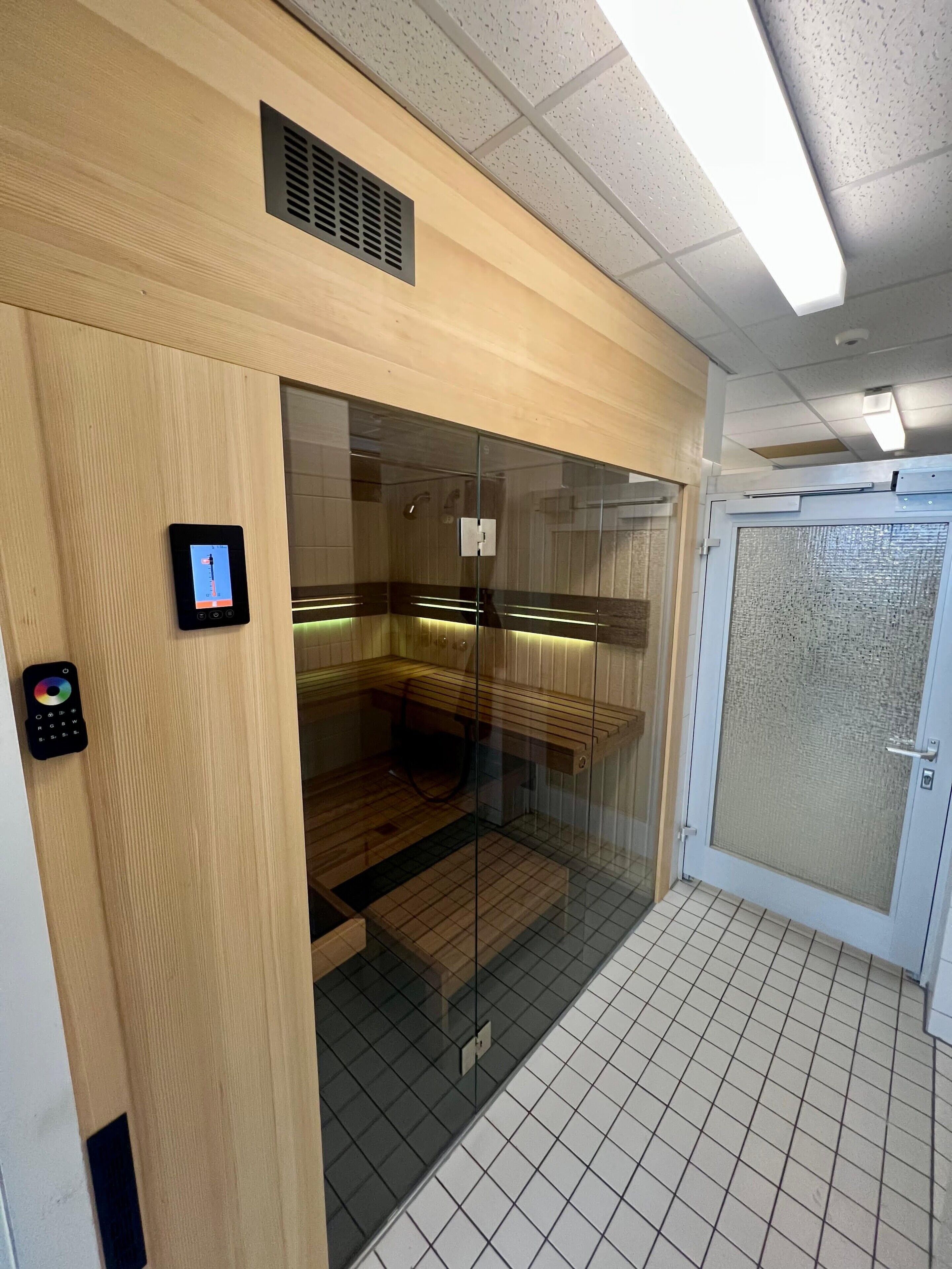 Um elevador moderno com painel de controle, cabine de vidro e piso revestido de azulejos.