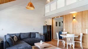 Un salon moderne avec un canapé d’angle, un coin repas avec des chaises blanches, un mur d’accent en bois et une cuisine en arrière-plan.