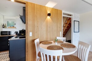 A modern kitchen with a dining area, wooden wall paneling, and a staircase.