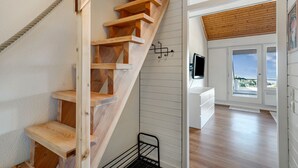 Un escalier en bois menant à un balcon avec vue, un mur blanc sur lequel est fixé un téléviseur et un plancher en bois.