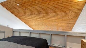 Ein Schlafzimmer mit schrägem Dach, einem Bett, einer Kommode und einem Fenster.