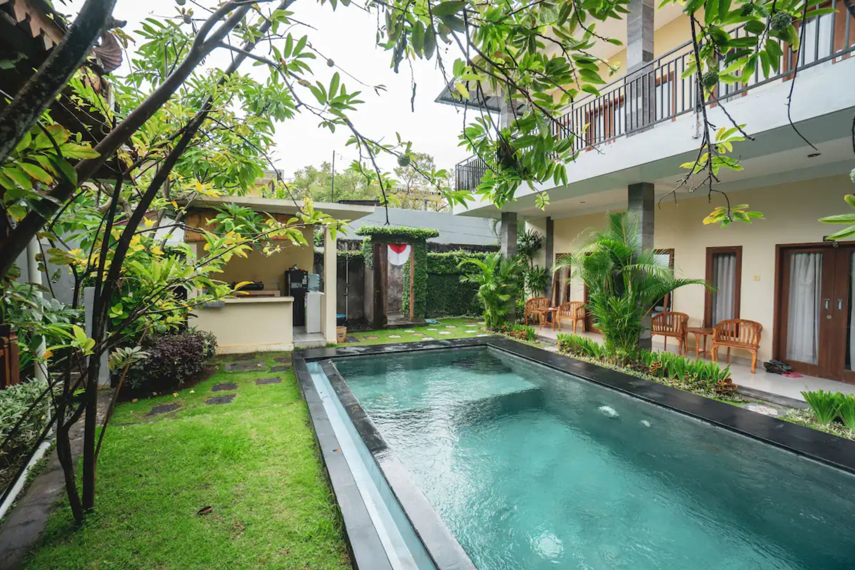 A swimming pool surrounded by lush greenery and a two-story building with outdoor seating.