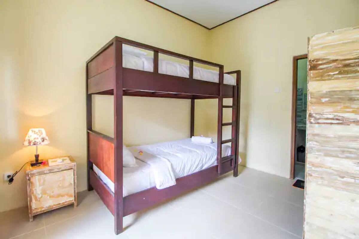A bunk bed with a ladder, a bedside table with a lamp, and a plain wall.
