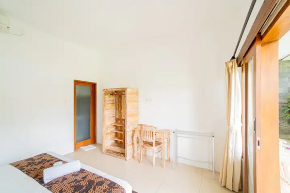 A room with a bed, a wooden chair, a small table, and a sliding glass door leading to an outdoor area.