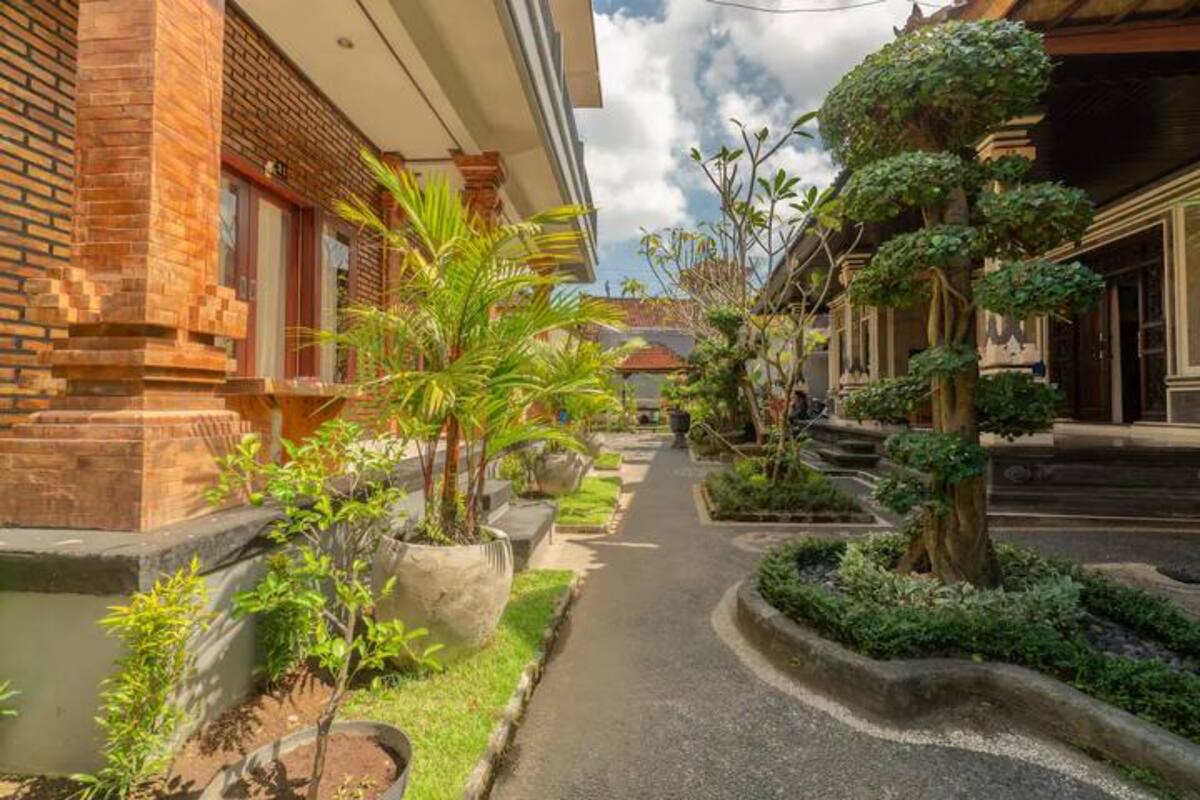 A narrow pathway flanked by brick buildings with potted plants and a small garden area.