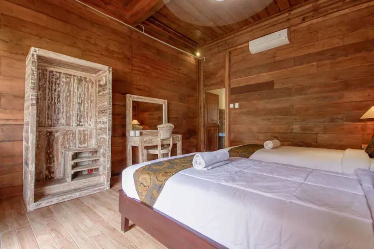 A wooden room with a bed, a chair, and a mirror.