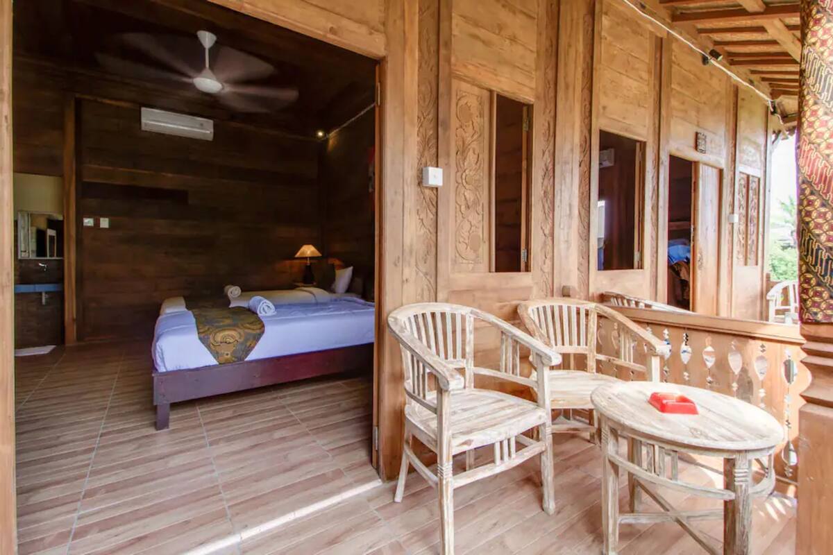 A wooden room with a bed, a chair, a table, and a balcony.