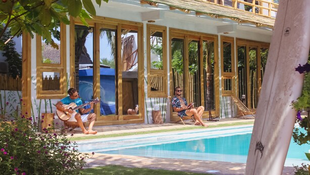 Zona junto a la piscina con sillas de madera, una piscina y un área de estar techada con ventanas amplias.