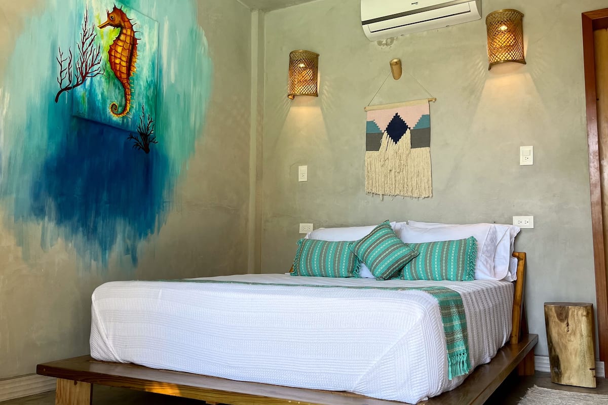 A bedroom with a bed, a seahorse mural, wall-mounted lights, and a macrame wall hanging.