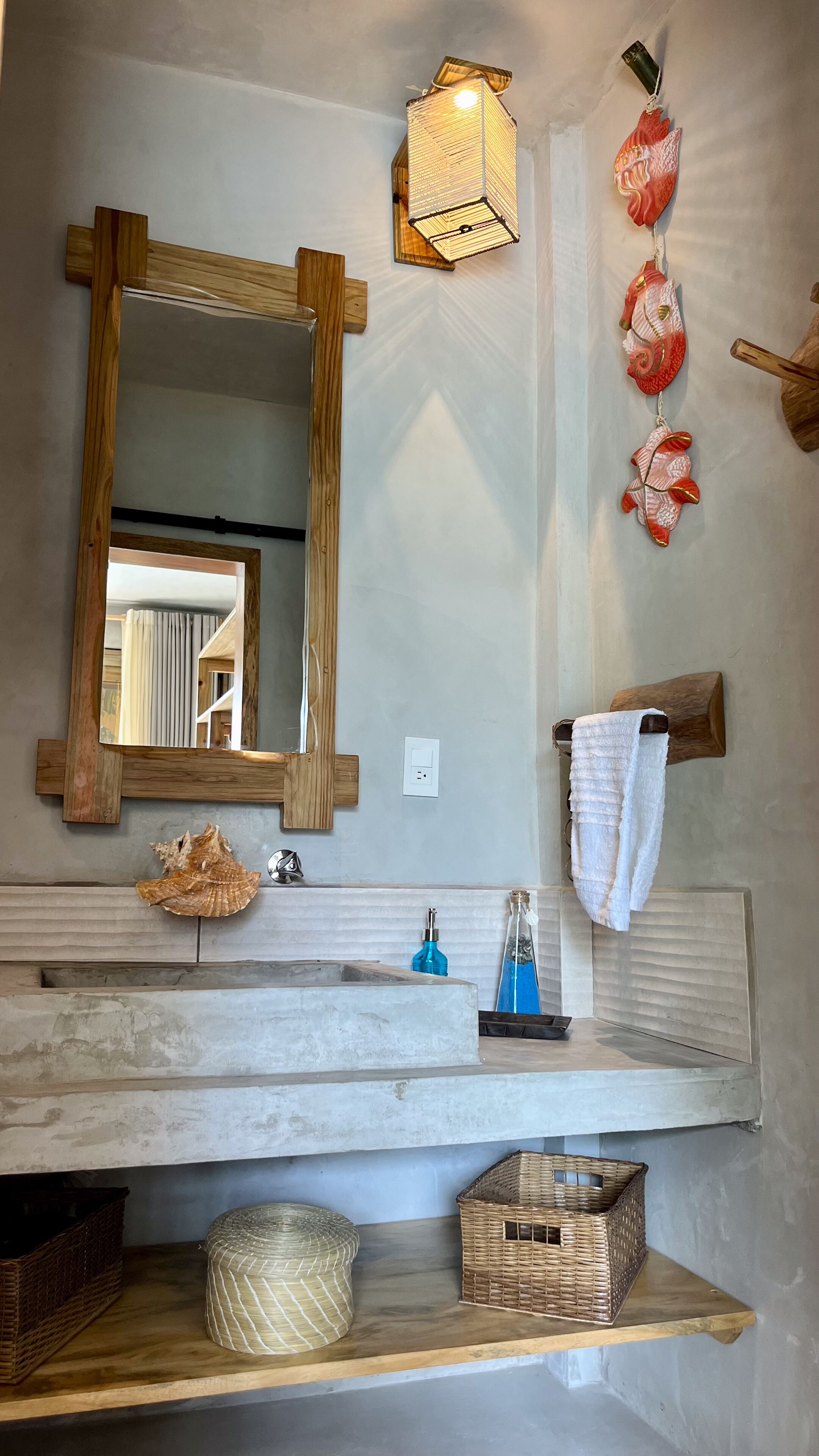 Un baño con tocador de madera, espejo, toallero, lámpara y conchas decorativas.