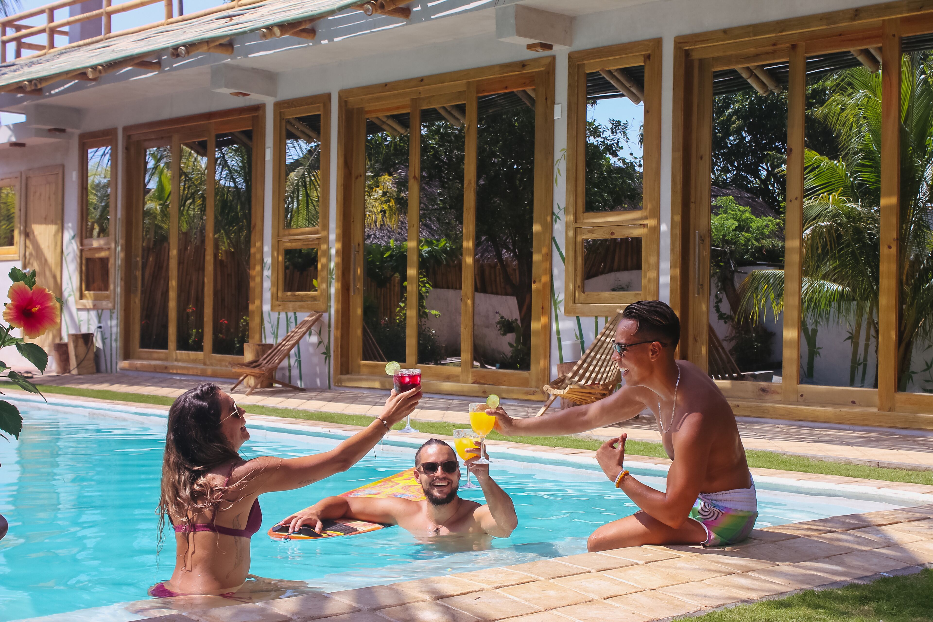 A poolside area with wooden deck, large windows, and a view of greenery.