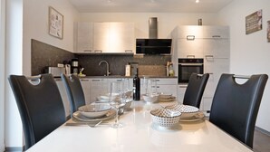 A modern kitchen with white cabinets, a black range hood, and a dining area with a white table set for four. - Holiday Home "Speicherhäuschen Maike" with Private Garden & Wi-Fi (Geeste)