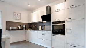 A modern kitchen with white cabinets, a stainless steel oven, a microwave, and a coffee maker. - Holiday Home "Speicherhäuschen Maike" with Private Garden & Wi-Fi (Geeste)