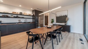 A modern kitchen with a wooden dining table and black chairs, a built-in oven, and a large window.