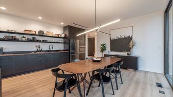 A modern kitchen with a wooden dining table and black chairs, a built-in oven, and a large window.