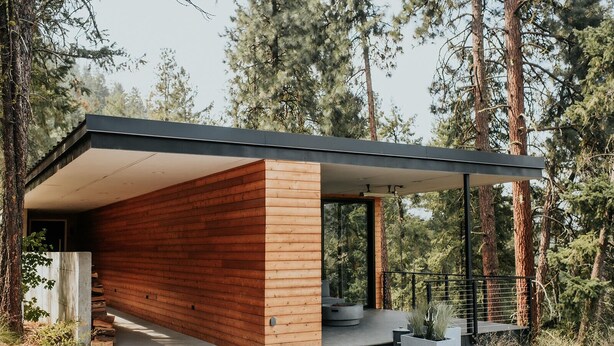 A modern cabin with a wooden exterior, a covered porch, and a concrete pathway leading to the entrance.