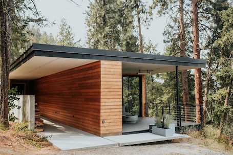 A modern cabin with a wooden exterior, a covered porch, and a concrete pathway leading to the entrance.