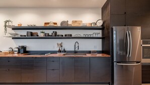 A modern kitchen with dark cabinetry, a stainless steel refrigerator, and wooden countertops.