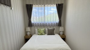 A neatly made bed with a white duvet, two bedside tables with lamps, and a window with curtains.