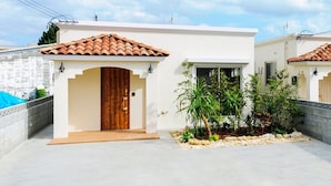 A modern house with a tiled roof, a wooden door, and a small garden with plants.