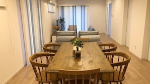 A dining area with a wooden table and chairs, a sofa, and a potted plant.