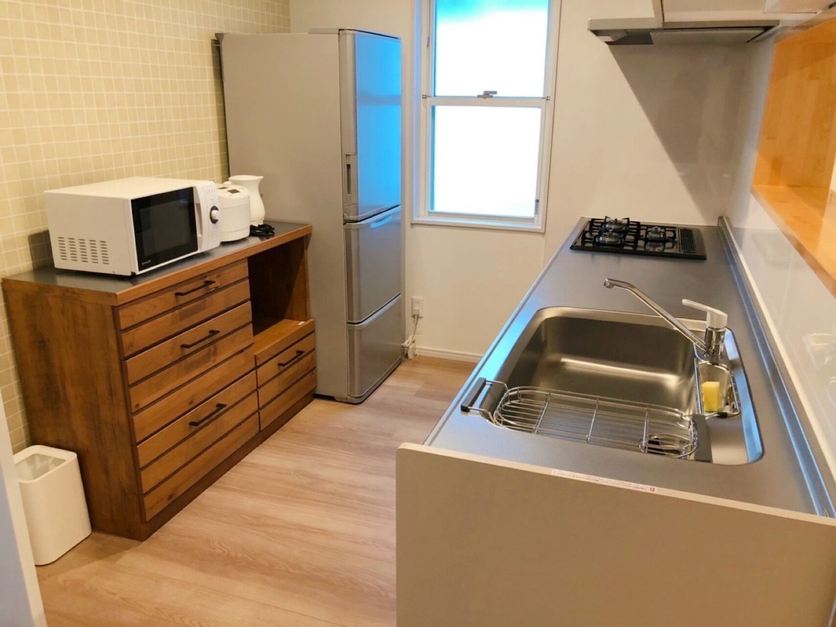 Una cocina compacta con microondas integrado, refrigerador de acero inoxidable, estufa a gas y pileta con dispensador de jabón.