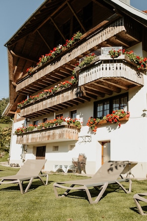 Un immeuble à plusieurs étages, doté de balcons ornés de fleurs, d’un espace extérieur aménagé pour s’asseoir et surplombant un ciel d égagé.