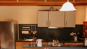 Een keuken met houten kastjes, een roestvrijstalen koelkast, een eettafel met stoelen en een hangende hanglamp.