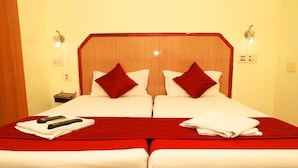 Una cama doble con ropa de cama roja, dos almohadas, un control remoto y una toalla doblada.
