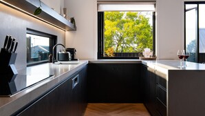 A modern kitchen with a large window, a built-in sink, and a countertop with kitchen utensils. - Maison Noire- stunning Scandinavian design, great location (Daylesford)