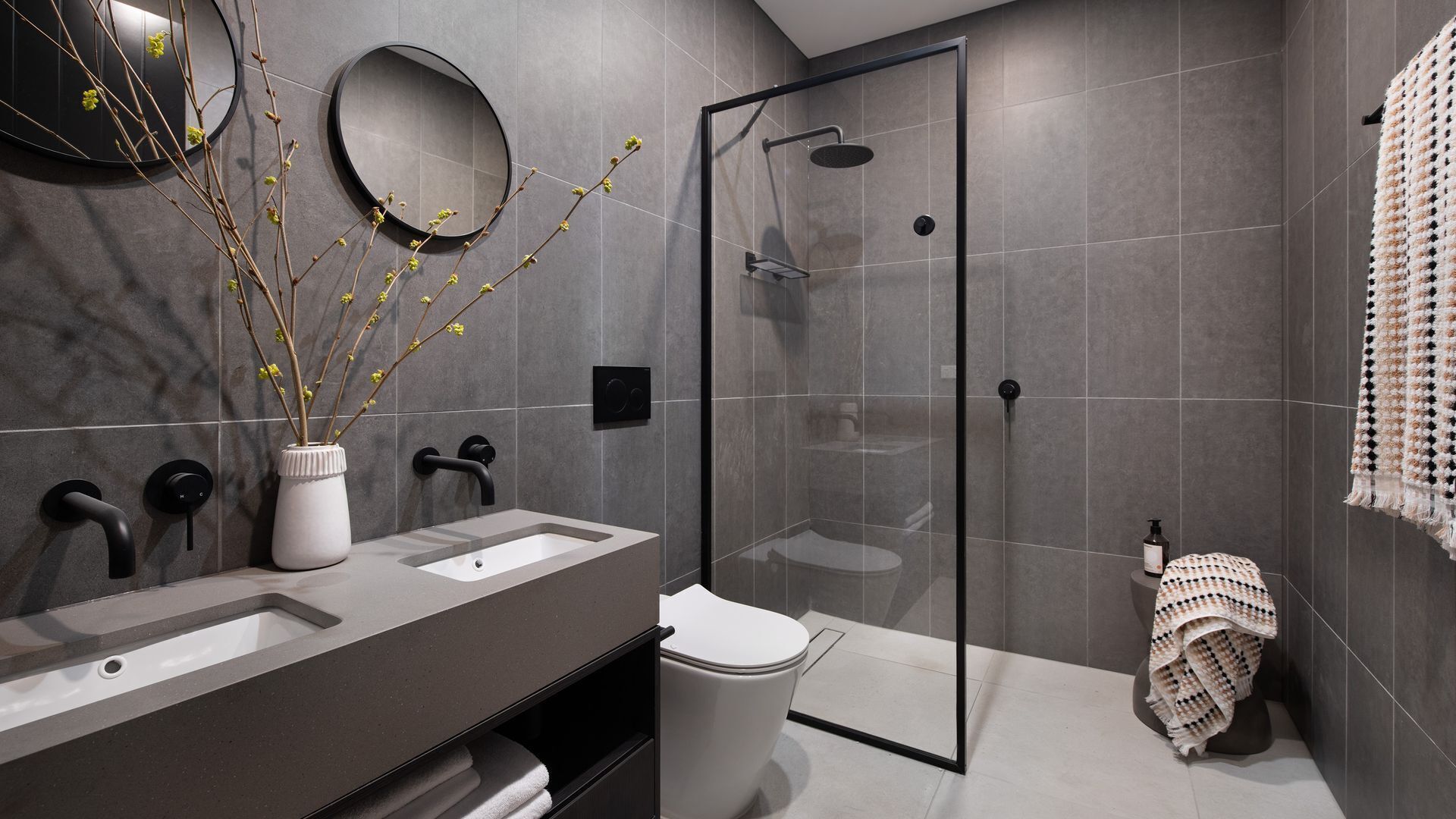 A modern bathroom with a glass-enclosed shower, a white toilet, and a vanity with two sinks.