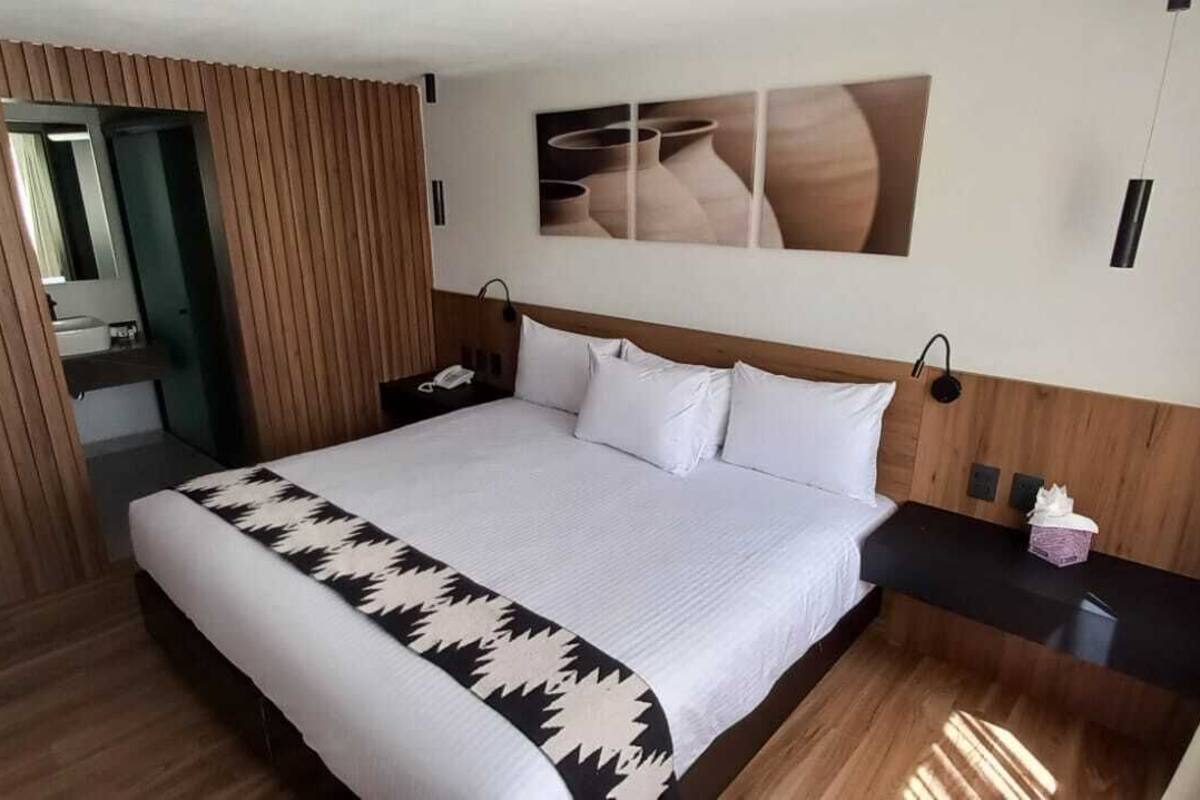 Une chambre d’hôtel avec un grand lit, une tête de lit en bois, une table de chevet avec une lampe, un téléviseur fixé au mur et un mur recouvert de panneaux de bois.