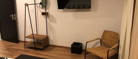 Quarto com cama, uma cadeira, televisão fixada na parede e uma porta.