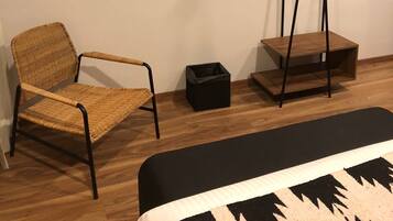 Ein modernes Zimmer mit einem Wand-Fernseher, einem Korbstuhl, einer kleinen schwarzen Mülltonne und einem Nachttisch aus Holz mit Spiegel.