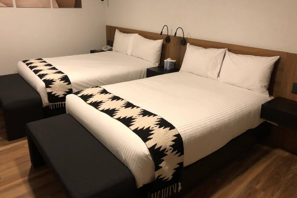 Une chambre double avec deux lits, chacun recouvert d’une courtepointe blanche et agrémenté d’oreillers assortis. Il y a des tables de chevet avec des lampes et une petite table entre les lits.