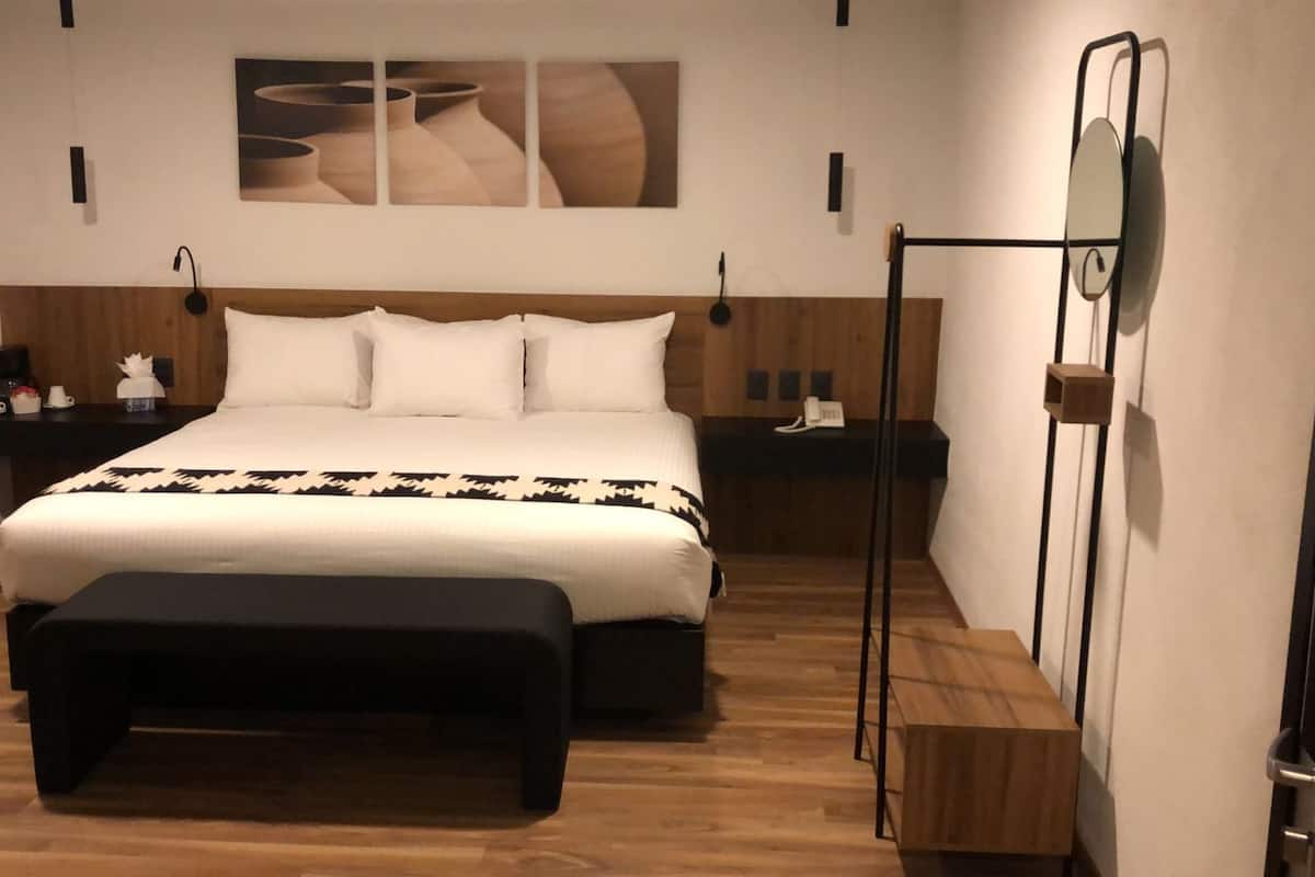 Une chambre moderne avec un grand lit, une tête de lit en bois, des tables de chevet, un banc et un téléviseur fixé au mur.
