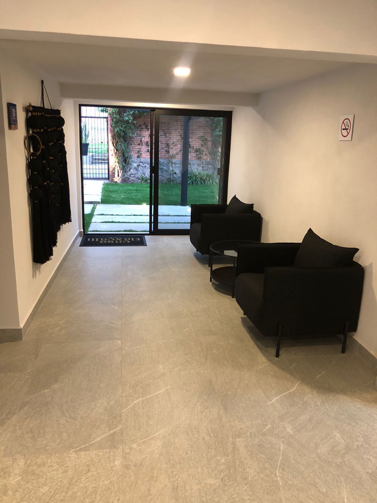 A modern living area with a black sofa, a small round table, and a sliding glass door leading to a garden.