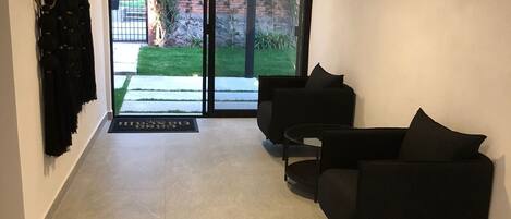 A modern living area with a black sofa, a small round table, and a sliding glass door leading to a garden.